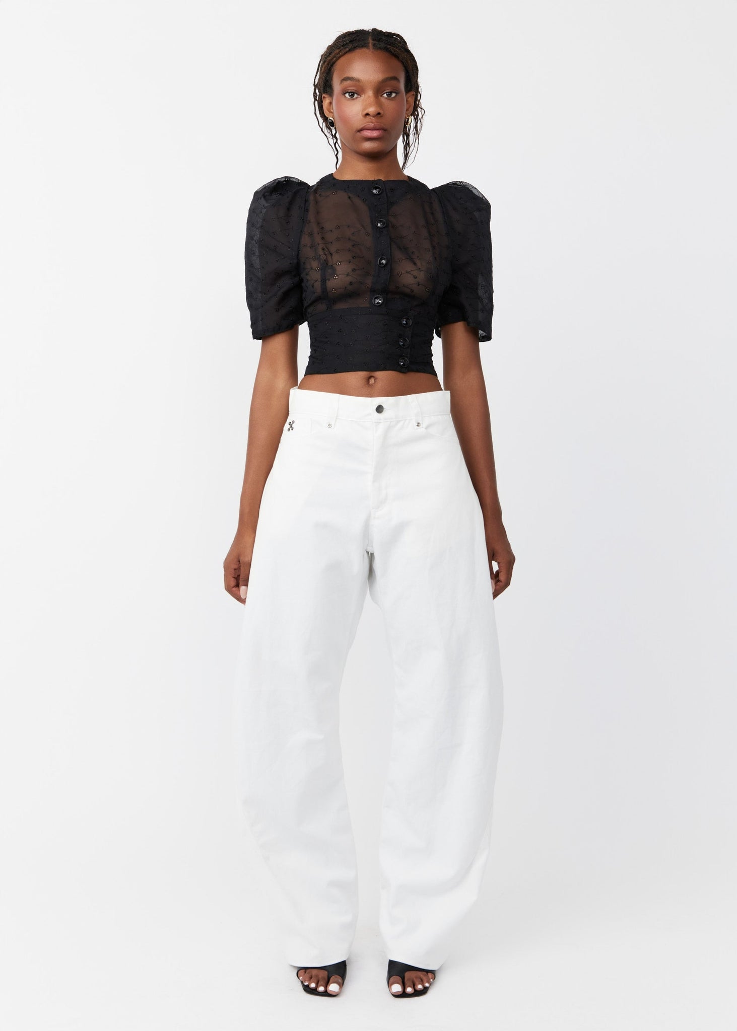 Woman wearing a black top with puff sleeves and white pants on a white background